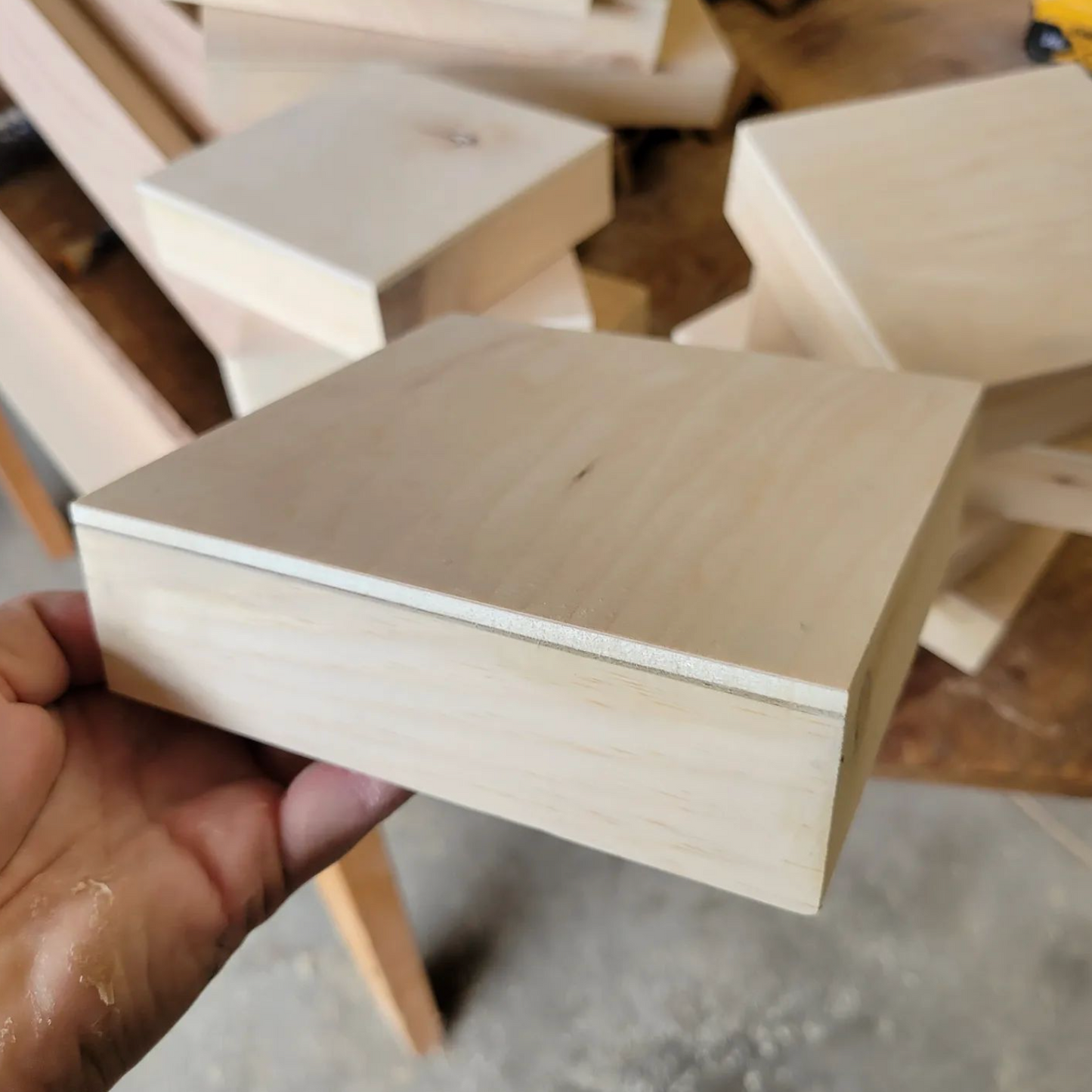 A hand holding a beige wooden cradled panel.